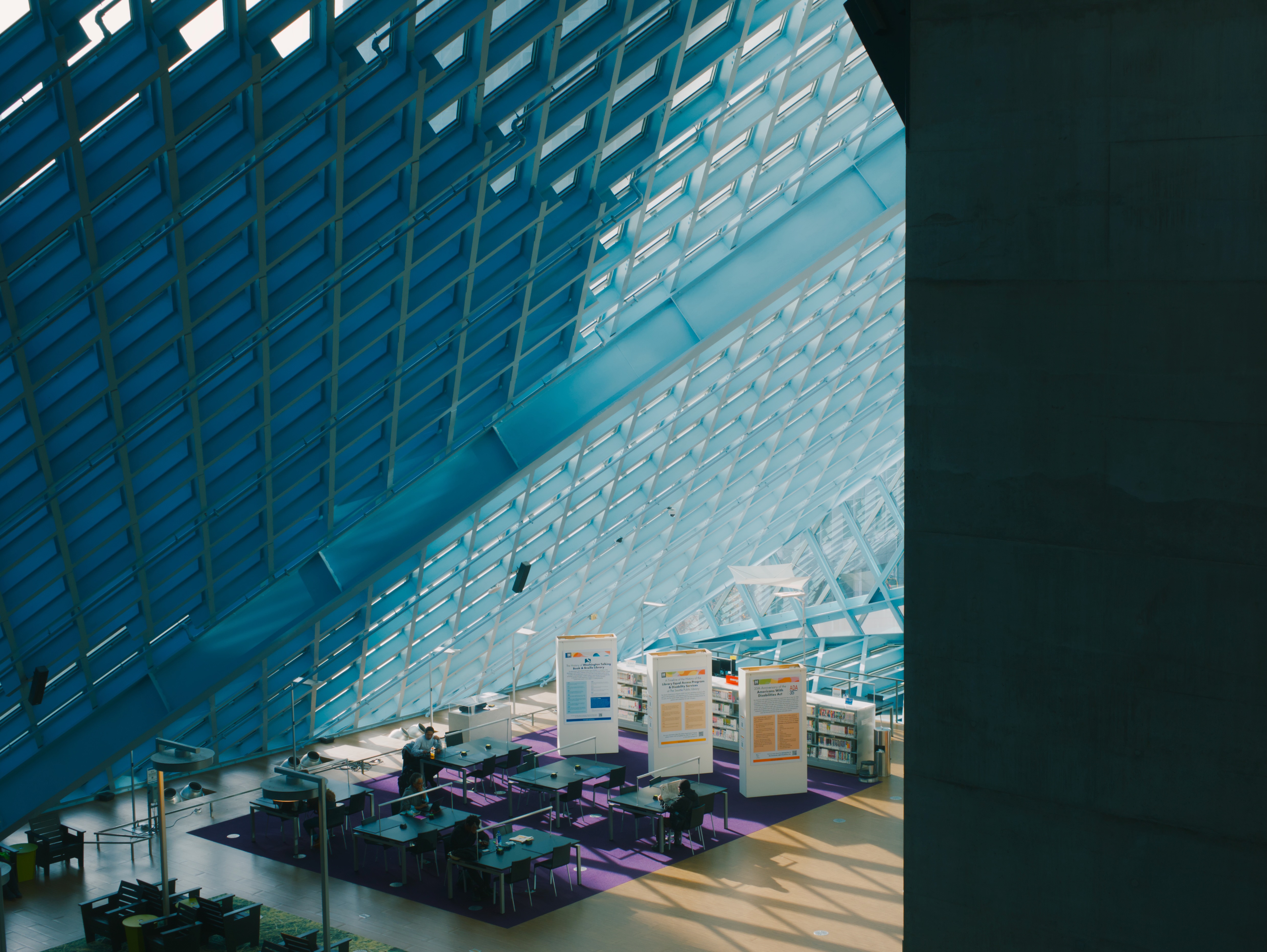 Library lobby with geometric glass and metal architecture features. Purple seating below dramatic angular skylights casting geometric shadows on the floor.